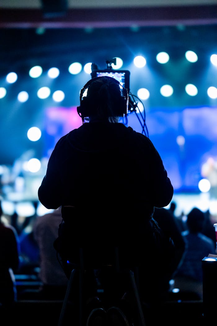 Silhouette of a camera operator filming a live concert with bright stage lights.