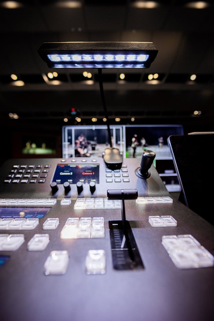 Contemporary shiny audio mixer controller with buttons and switches under illuminated lamp in modern studio